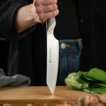 Global Kiritsuke 15cm standing vertically with a chef holding it up, indented to a wooden chopping board