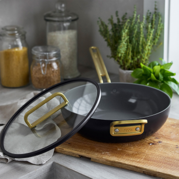 Pan with lid resting on edge, placed on a wooden chopping block on a kitchen bench.