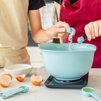 two spoons pouring ingredients into a mixing bowl.
